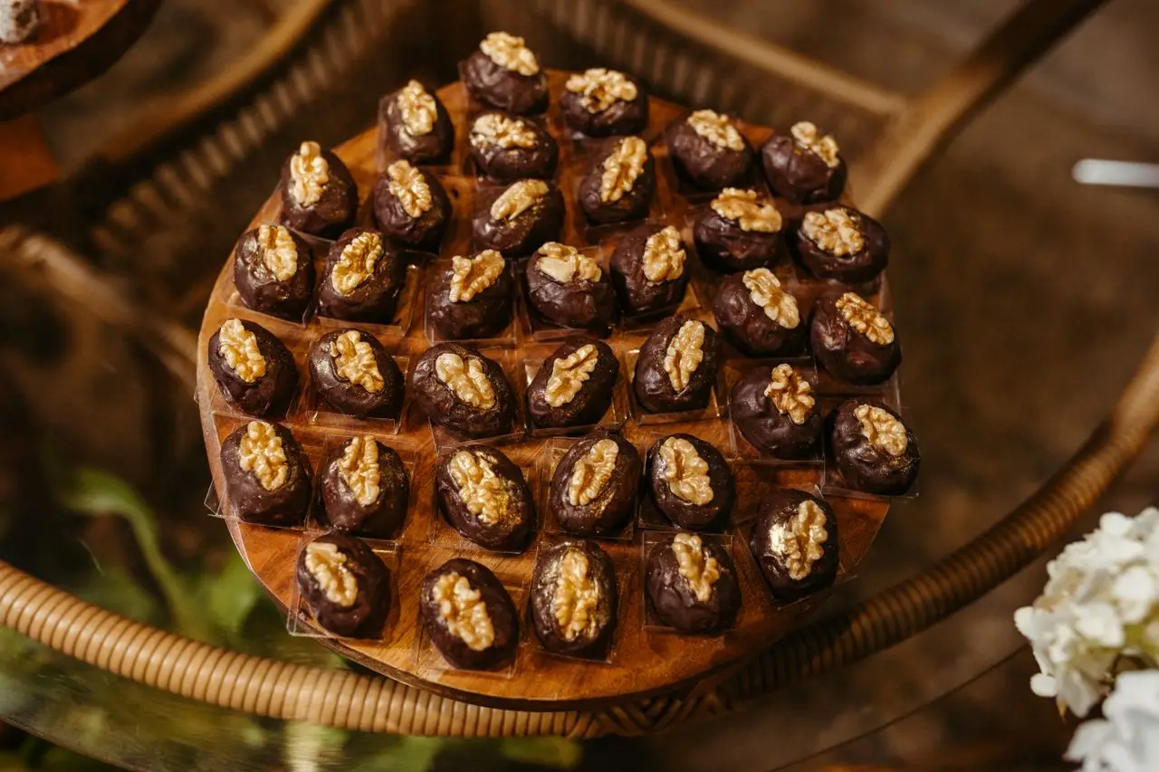 A tempting array of chocolate-covered date bites topped with walnuts on a wooden tray.