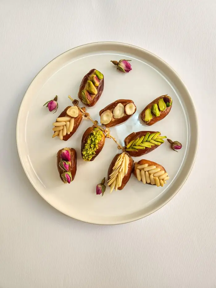 A plate of gourmet stuffed dates with pistachios, almonds, and rosebuds elegantly arranged on white.