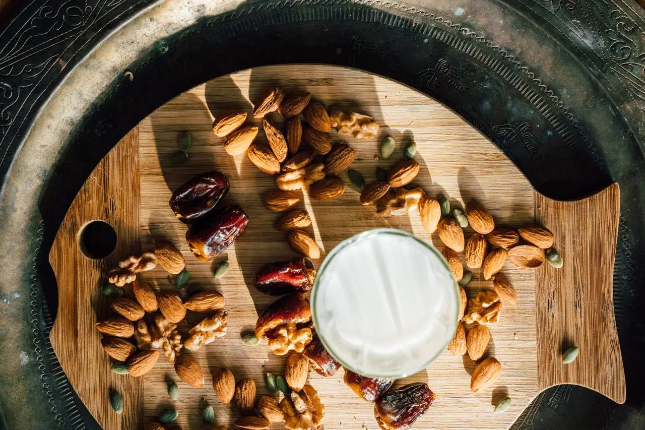 delivery-policy Flat lay of almonds, dates, and milk for iftar on a wooden board.